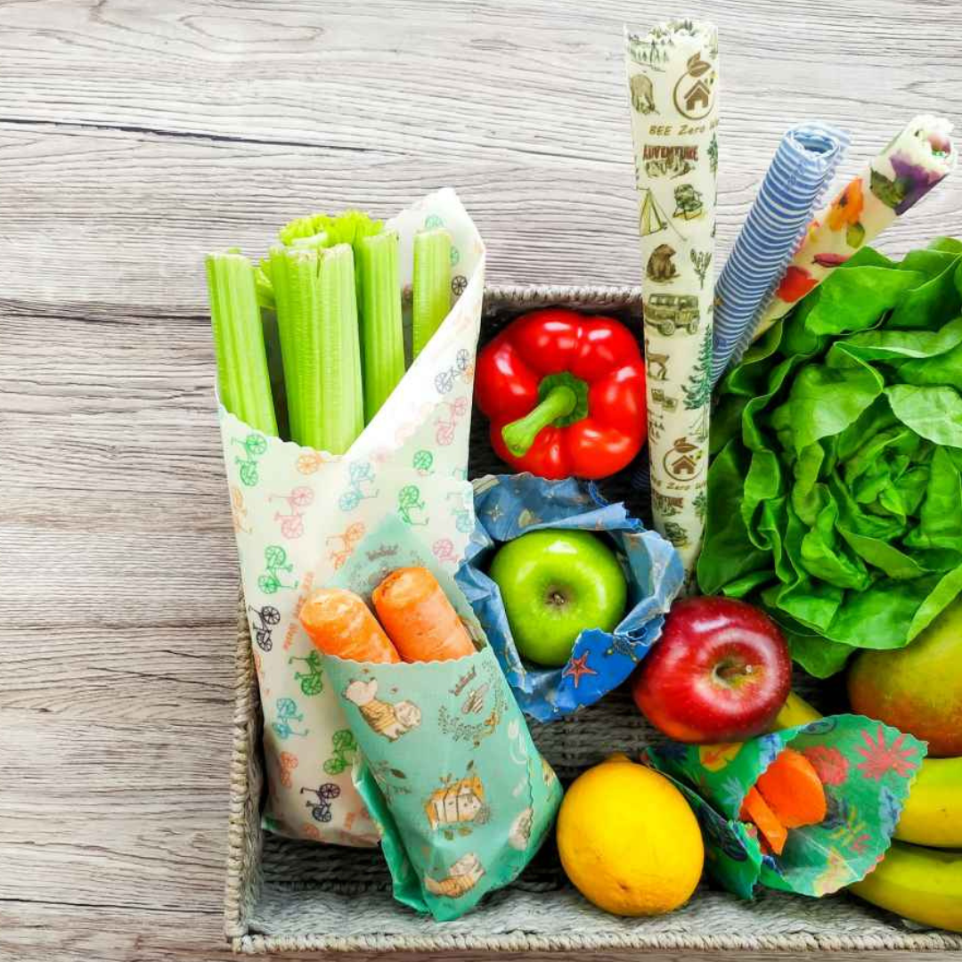 Assorted beeswax and vegan wax food wraps in vibrant patterns, covering bowls and wrapping fresh produce, showcasing an eco-friendly alternative to plastic wrap.