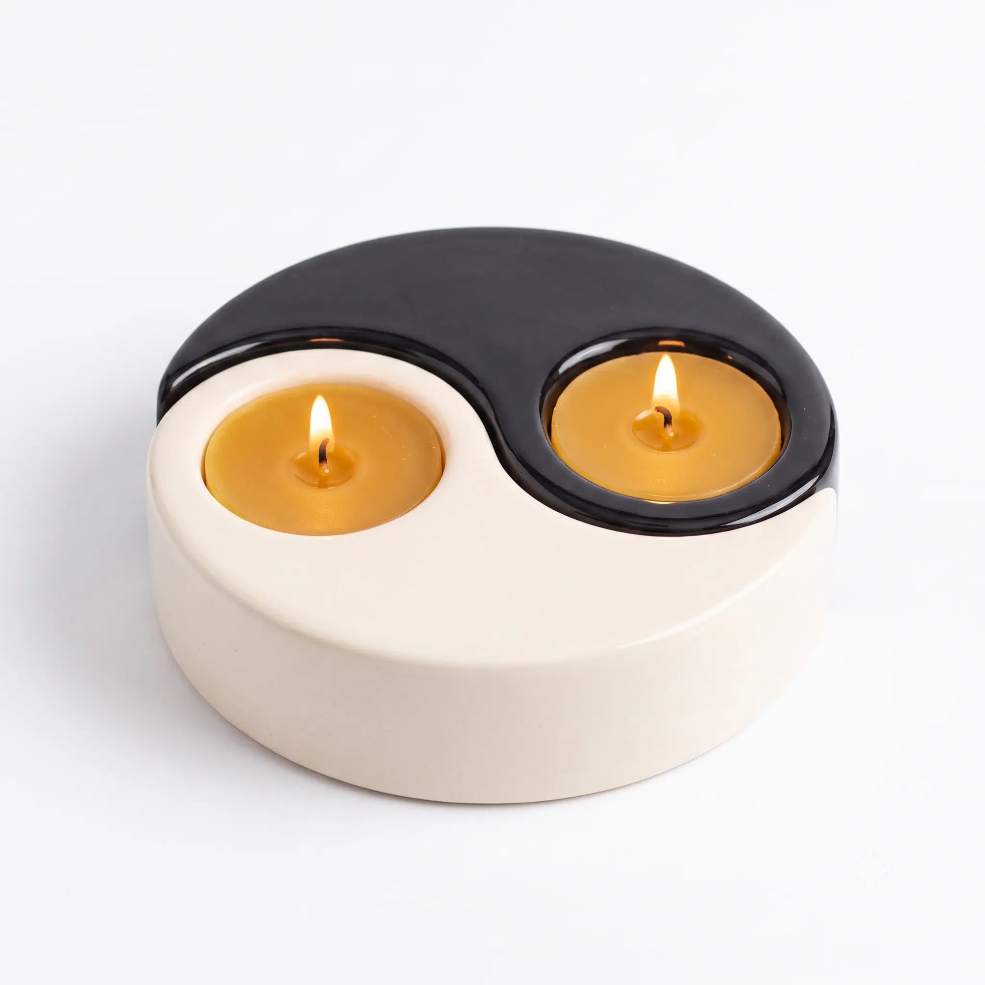 Black and white ceramic Yin Yang tealight candle holder fitted snug with two natural yellow beeswax tealight candles on a clean white background.