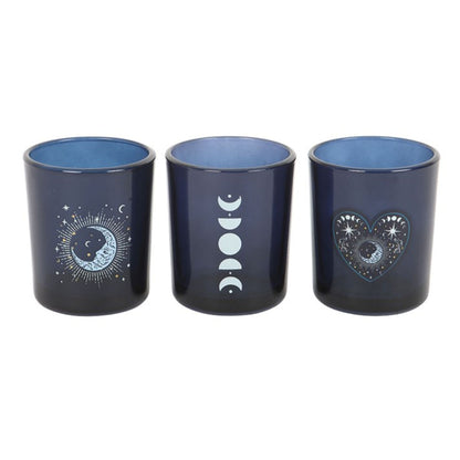 Close-up of three blue glass votive holders featuring white decals of a star-filled heart, a column of moon phases, and a moon-sun combination.