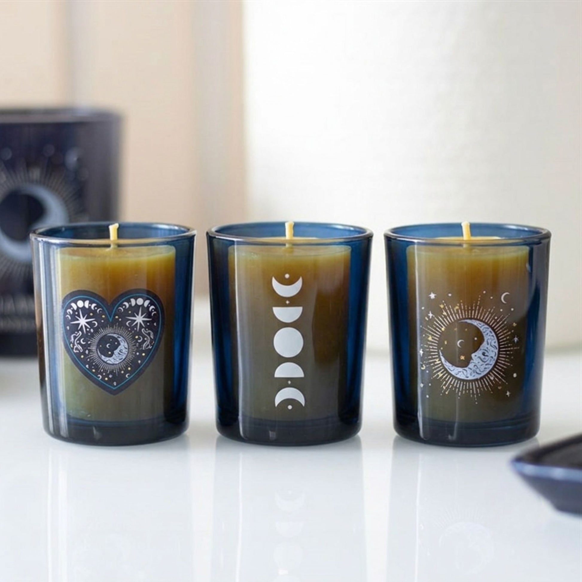 Set of three cobalt blue glass tea light holders with various silver celestial and astrological patterns, shown with wicks against a plain white background