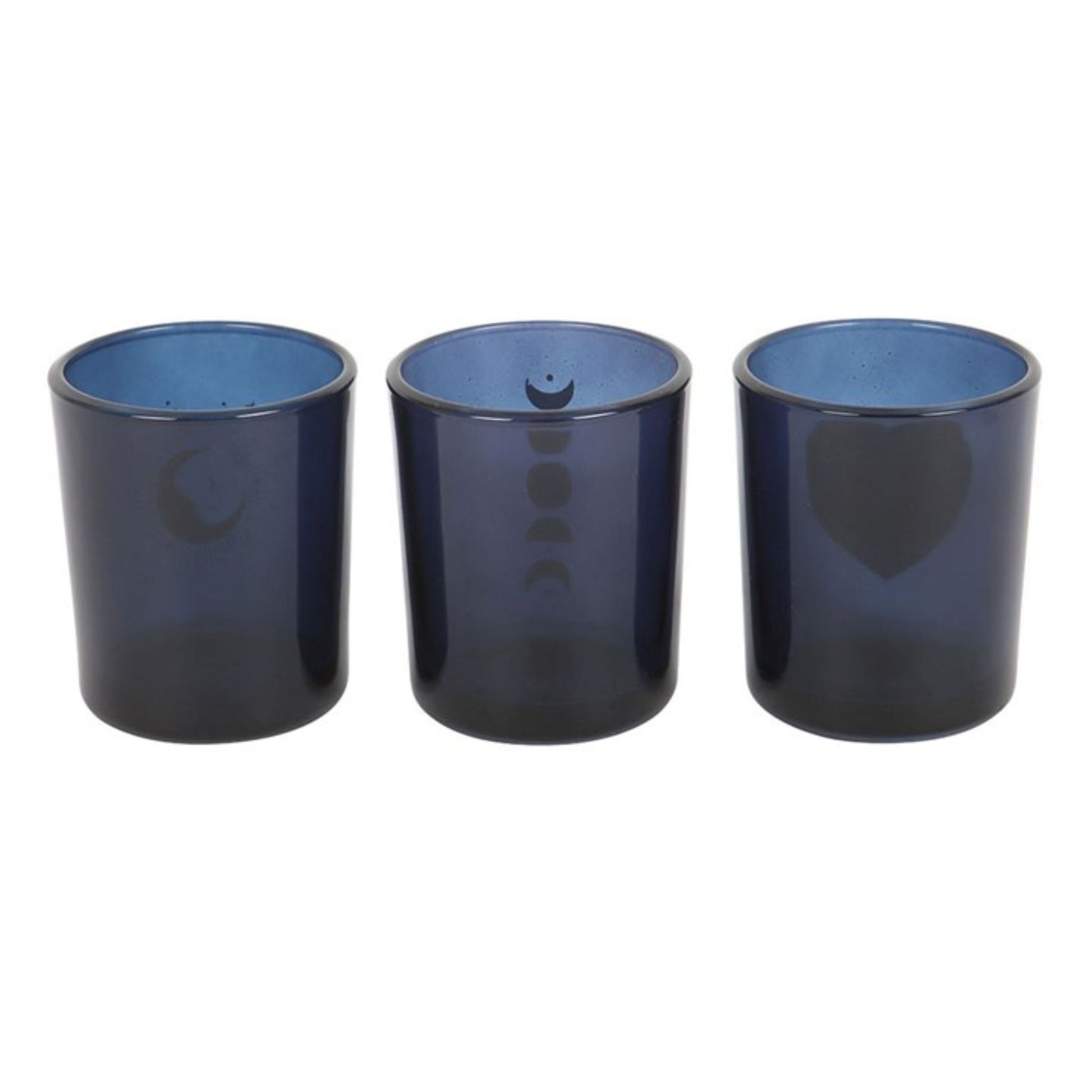 Three deep blue glass candle holders with mystical and spiritual designs, including moon phases and a sun, arranged in a row with unlit beeswax votive candles.