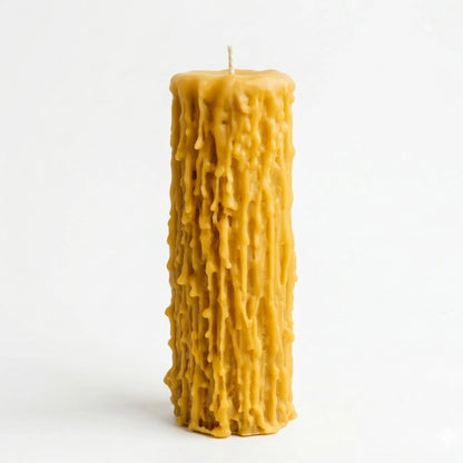 A well-organized, close-up photograph of five beeswax pillar candles arranged by increasing height on a light-colored surface. The two shortest candles are in sharp focus, showcasing their unique dripped, highly textured natural yellow wax.