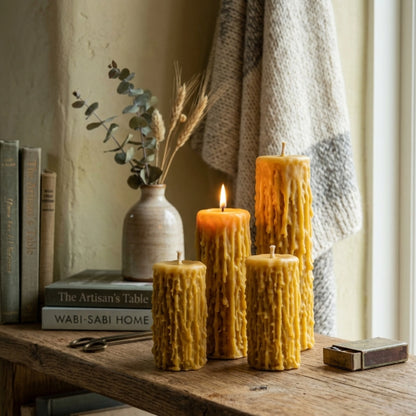 A macro-style photo of an exceptionally tall beeswax pillar candle, completely enveloped in a dense, cascading layer of natural dripped wax. The image captures the deep golden-yellow color and intricate, complex texture from top to bottom against a soft-focus background.